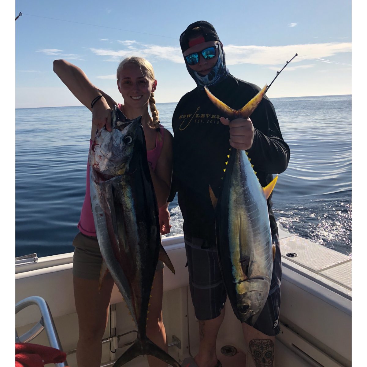 A man and woman holding up two fish on the boat.