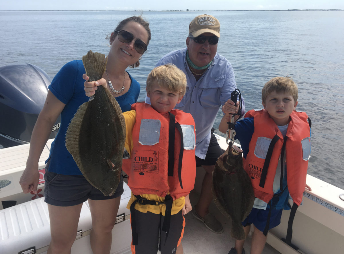 A family of four holding fish on the boat.