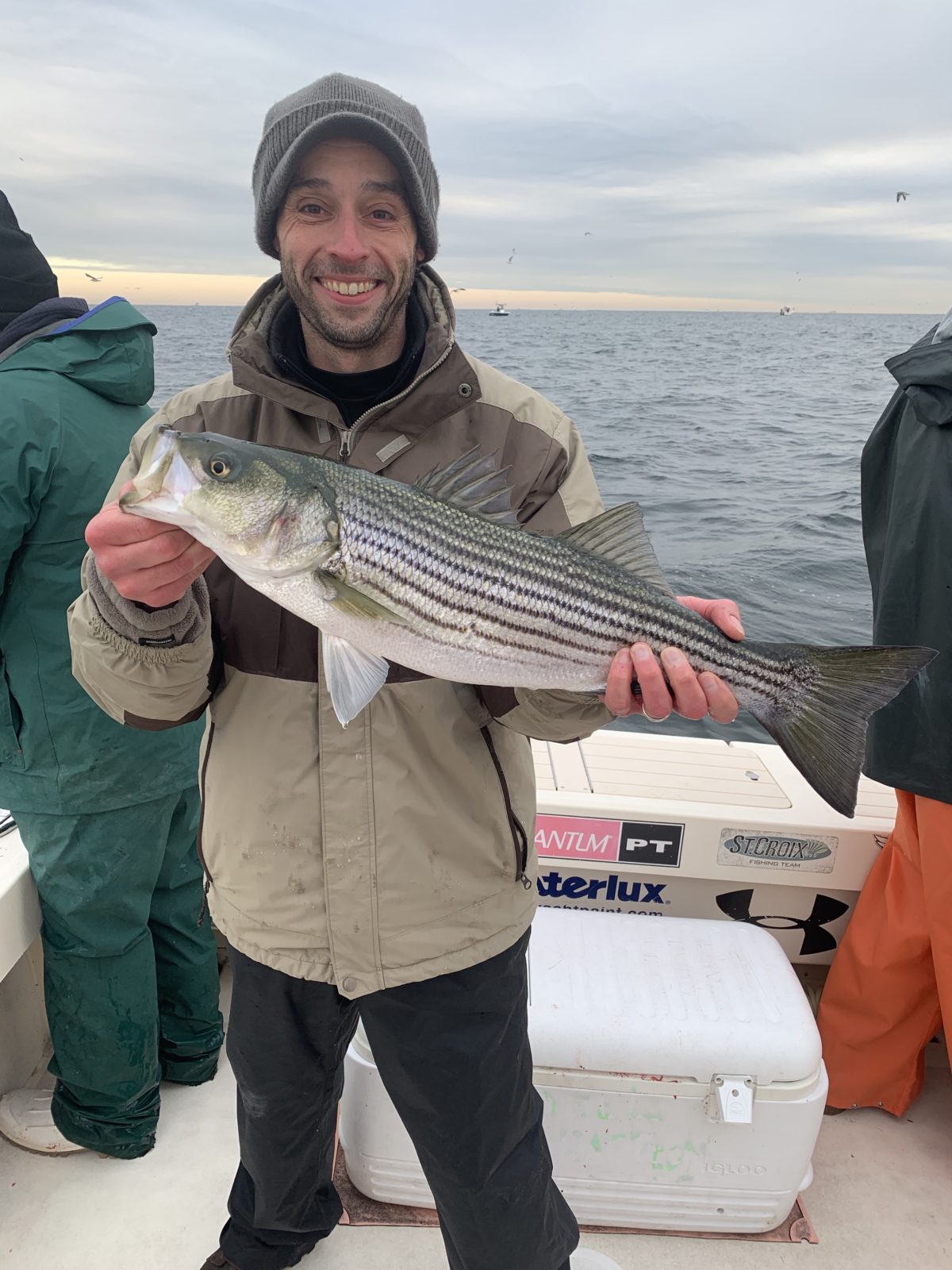 A man holding a striped fish on top of a boat.