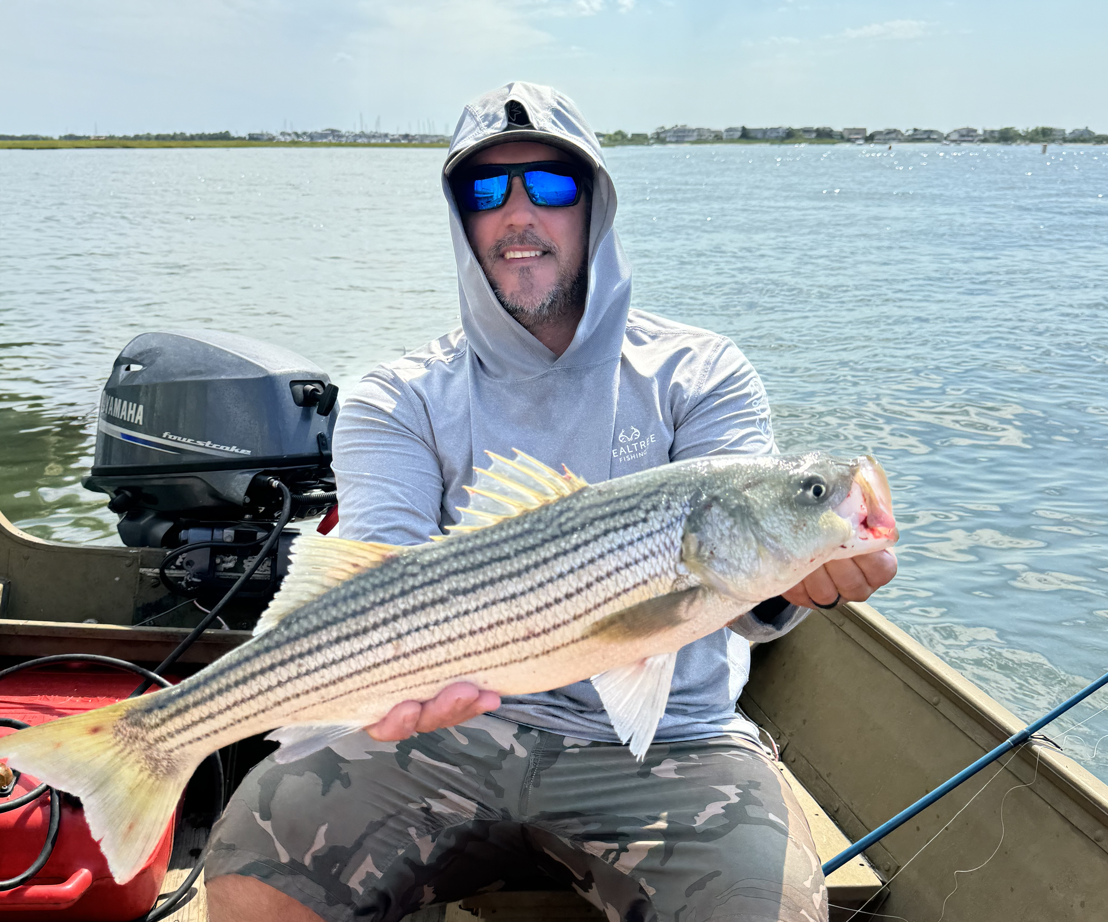 A man holding a striped fish while sitting in a boat.